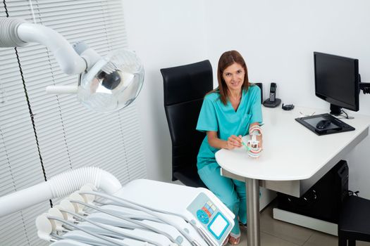 Portrait of happy female dentist explains how to brush your teeth at desk