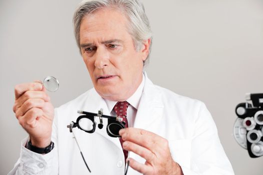 Skilled optometrist examining the lens while holding trial frame for an eye checkup