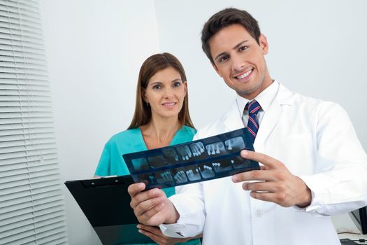 Portrait of happy dentist with dental nurse analyzing X-ray report in clinic