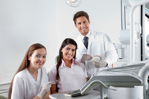 Portrait of happy young dentist and nurse with patient in clinic