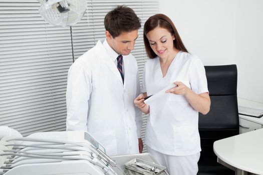 Male dentist with assistant discussing dental report in clinic