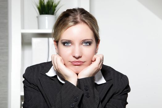 Young businesswoman sitting in her office thinking with her chin resting in her hands looking directly at the camera