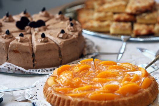 Dessert buffet at a wedding reception with an assortment of delicious freshly baked cakes and biscuits with focus to a colourful peach tart in the foreground