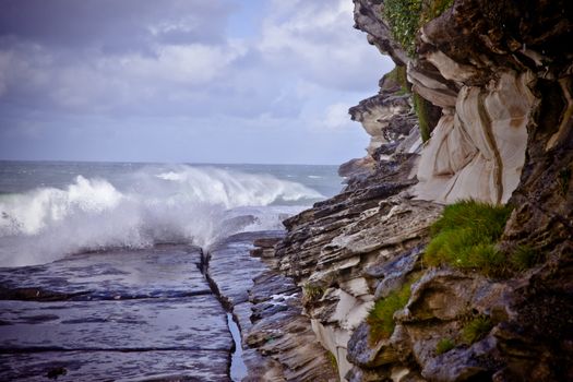 Waves breaking on a rocky ledge at the base of steep coastal cliffs