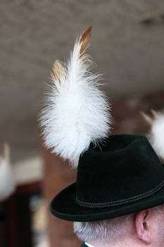 Elderly man weariing a decorative cockade of feathers attached to the side of his hat at a celebration or function