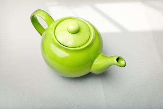 Green teapot on a table with shadow