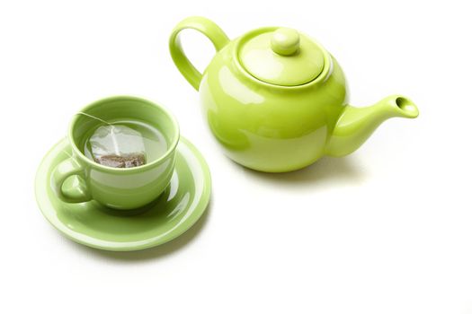 Green teapot and teacup with tea bag on a white textured photo. Natural colors