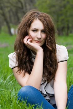 Beautiful and cute girl thoughtfully sitting on the green grass