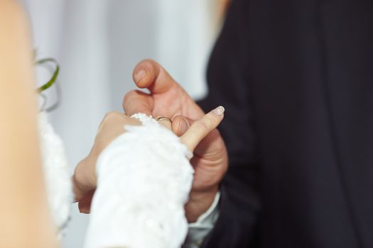 The groom puts the ring on the bride's hand.