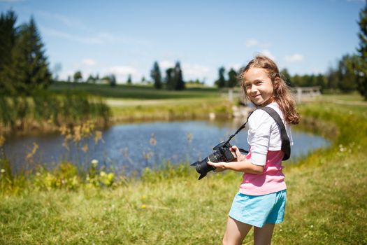 young photographer standing with a camera outside near a pond