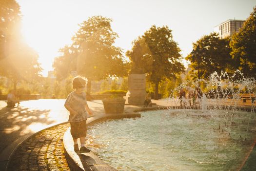 Boy standing by a fountain at sunset and getting wet