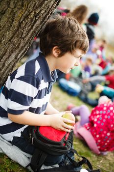 Boy sitting by a tree eating an apple on a school trip