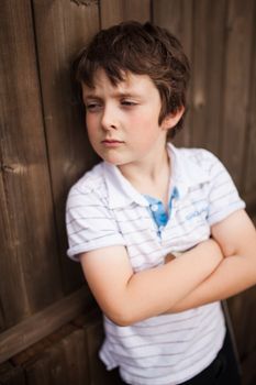 Sad little boy leaning on a wooden fence