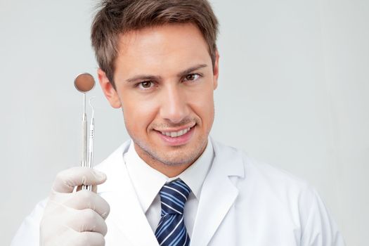Close-up portrait of happy male dentist holding angled mirror and carver in clinic