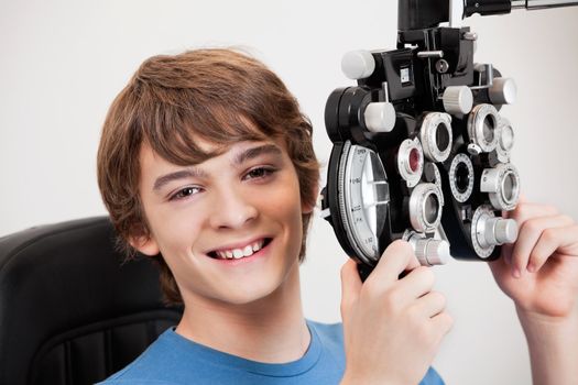 Smiling boy holding phoropter while undergoing an eye examination.