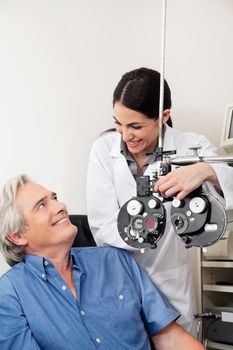 Caring eye specialist smiling at mature patient before performing eye test with phoropter