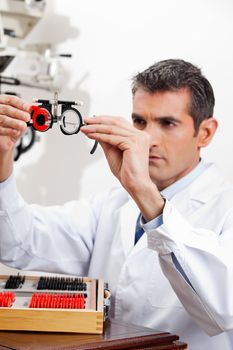 Optometrist checking the lens of trial frames with concentration for eye examination