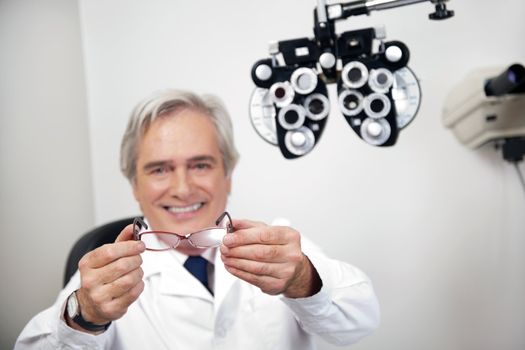 Portrait of smiling mature optometrist holding glasses at the clinic