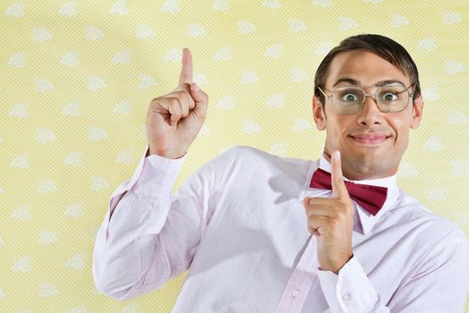 Portrait of young male geek pointing up over yellow textured background
