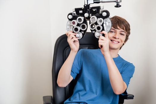 Teenager smiling while holding phoropter at the clinic