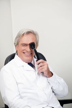 Smiling mature optometrist with ophthalmoscope for an easy view at retina