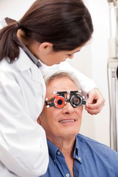 Female optometrist adjusting lens of trial frames on mature man