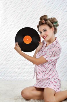 Portrait of young woman with hair curlers holding an old vinyl record while sitting on rug