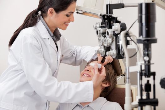 Smiling young optometrist putting eye drops in eyes of patient for clear vision