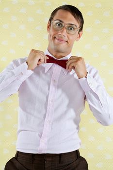 Portrait of a funny male geek adjusting bowtie over yellow textured background
