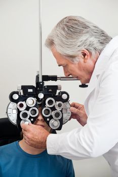 Mature experienced optometrist performing eye checkup with phoropter
