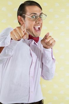 Portrait of an excited young geek with mouth open pointing at you over yellow textured background