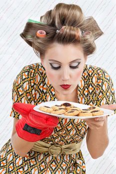 Young woman in dress with hair curlers smelling a plate of fresh baked cookies
