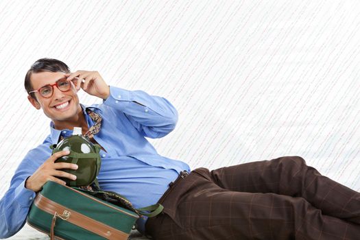 Portrait of happy geek businessman lying down with travel bag on textured background