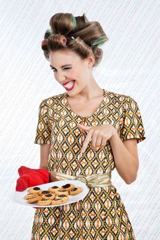 Portrait of young woman in a patterned dress winks as she points to the plate of baked cookies