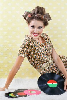 Portrait of young woman in a patterned dress wearing hair curlers while sitting with vinyl record