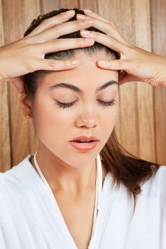 Close up of young woman in bathrobe holding her head in pain