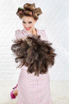 Portrait of happy young woman with hair curlers holding an ostrich feather duster