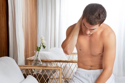 Young shirtless man suffering with neck pain while sitting at health spa
