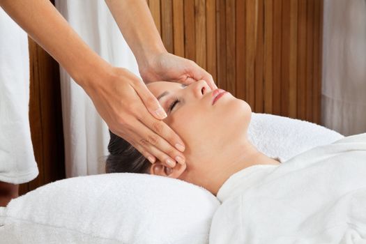 Young woman receiving head massage by masseur at health spa