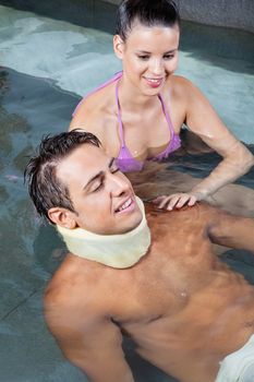 Young man wearing neck brace in pool with beautiful woman