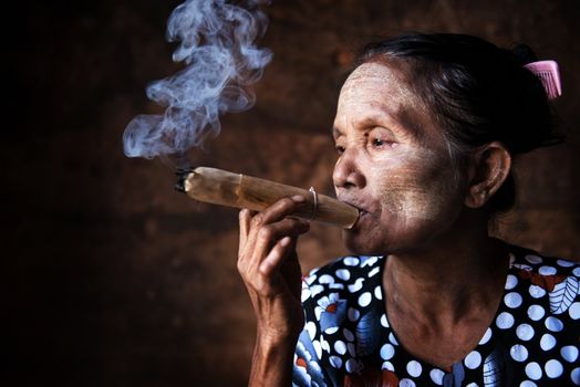 Old wrinkled Asian woman smoking traditional tobacco. Bagan, Myanmar.