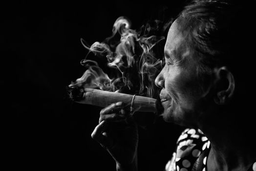 Old wrinkled Asian woman smoking traditional tobacco in monotone, black and white portrait. Bagan, Myanmar.