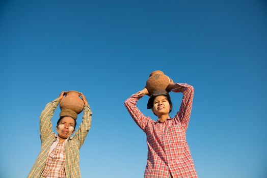 Asian traditional farmers carrying clay pot on head going back home, Bagan, Myanmar