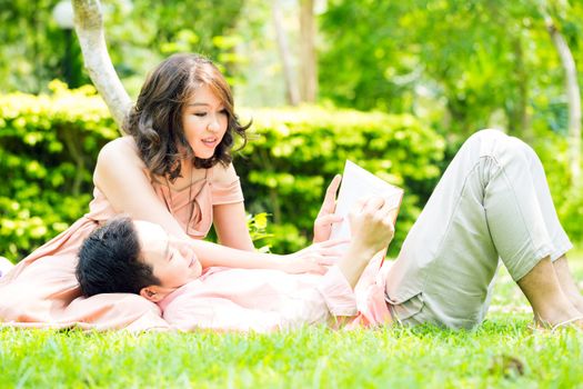 Couple relaxing in the garden, young man reading a book and resting on his girlfriend lap