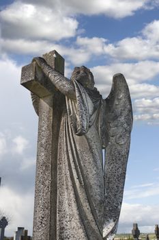 Angel statue embracing a cross and celtic graveyard in Ardmore county Waterford, Ireland with added grain