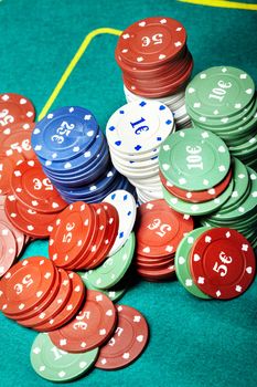 Vertical close-up photo of the various casino chips on a green table