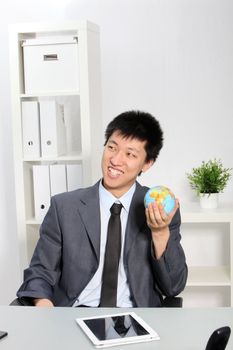 Young Asian businessman with a small globe seating in front of a tablet