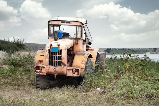 Old tractor outdoors at the field near the water. HDRI photo with natural colors