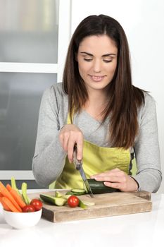 Beautiful woman cutting cucumber and vegetables in kitchen