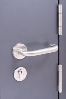Door handle and lock with stainless hinges on a steel grey door focus on the lock 